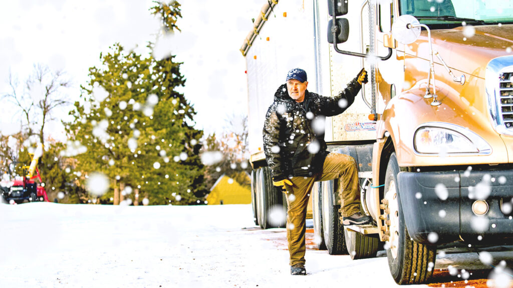 Man climbing into the cab of a semi truck as snow falls